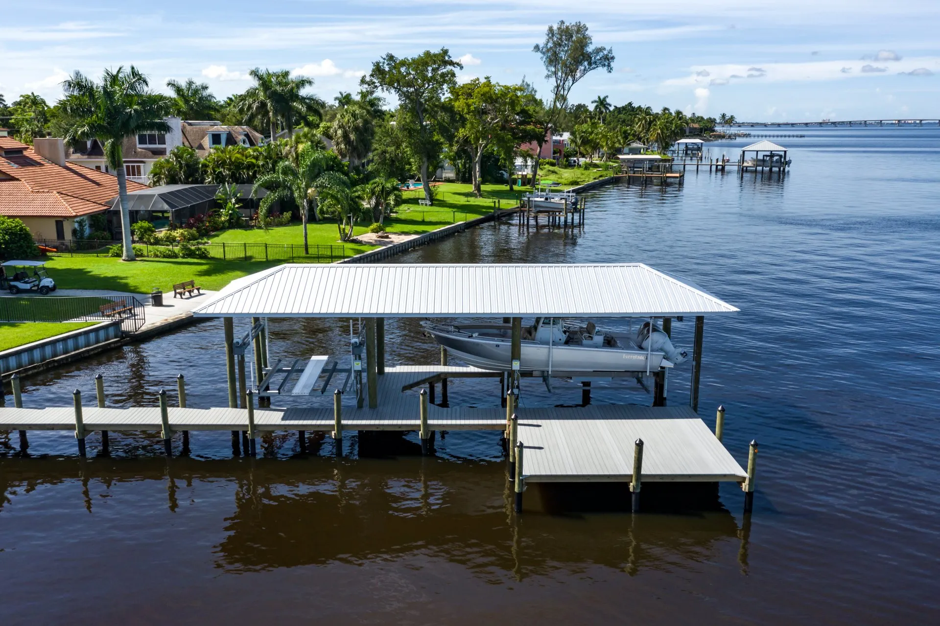 A dock with a boat lift featuring a covered roof, surrounded by lush greenery and waterfront homes.