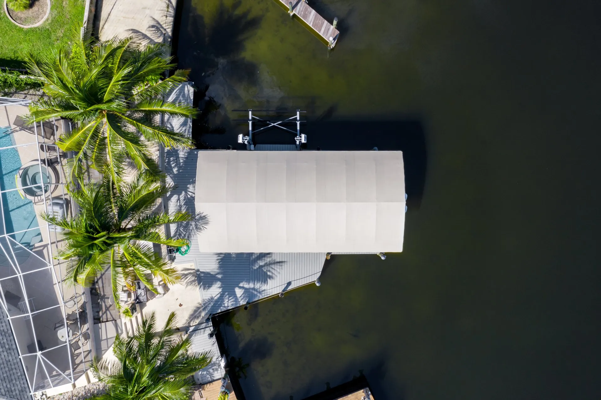 Aerial view of a boat lift with a canopy surrounded by palm trees and a waterfront dock.