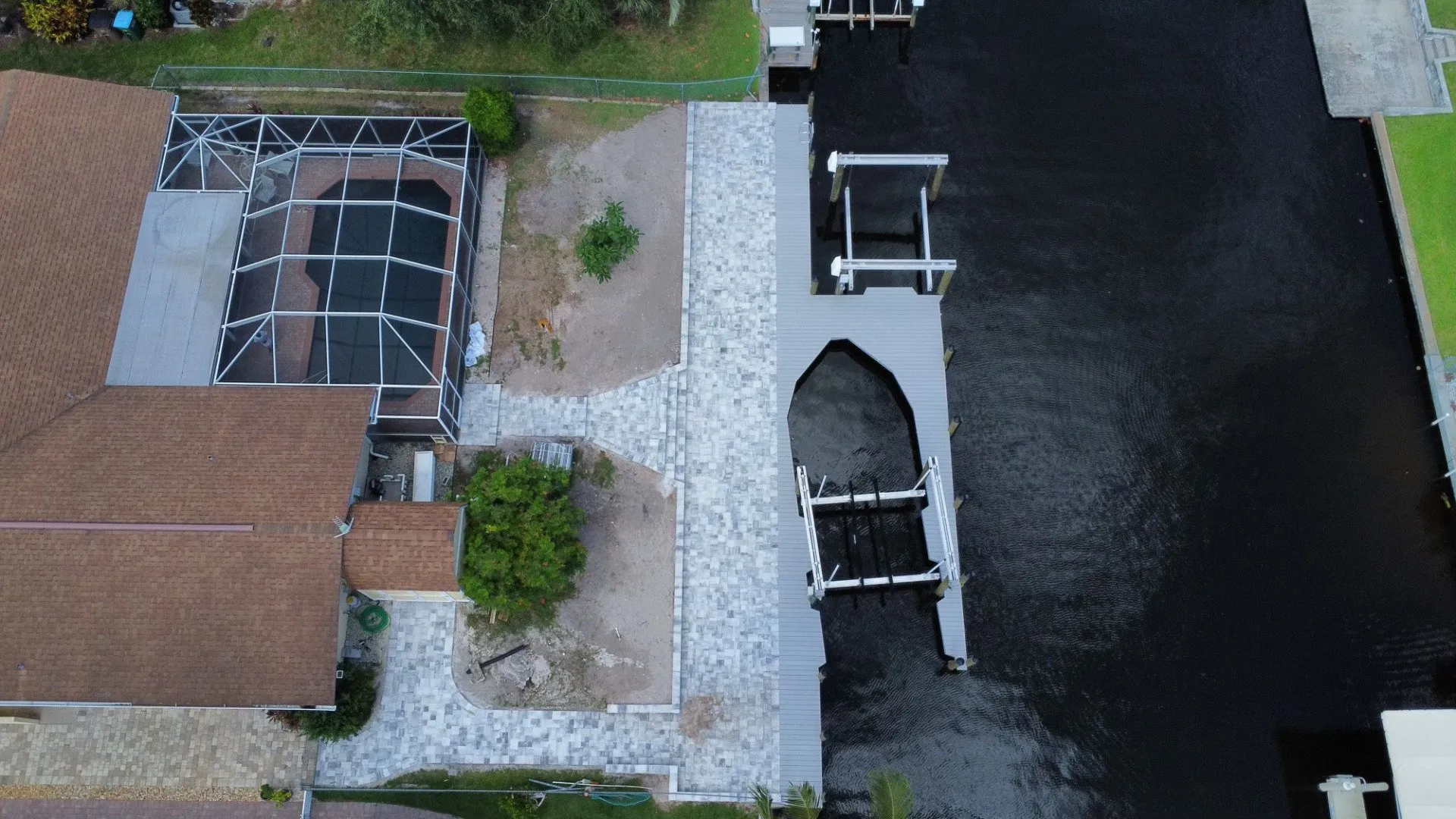 Aerial view of a residential property with a paver patio, screened pool area, and custom dock on a canal.