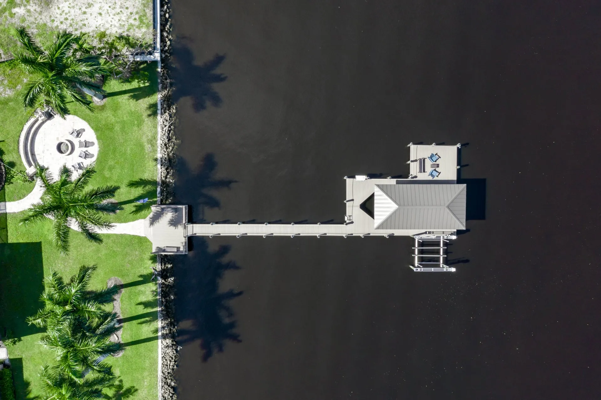 Aerial view of a dock with a pavilion and a firepit area on a lush green lawn