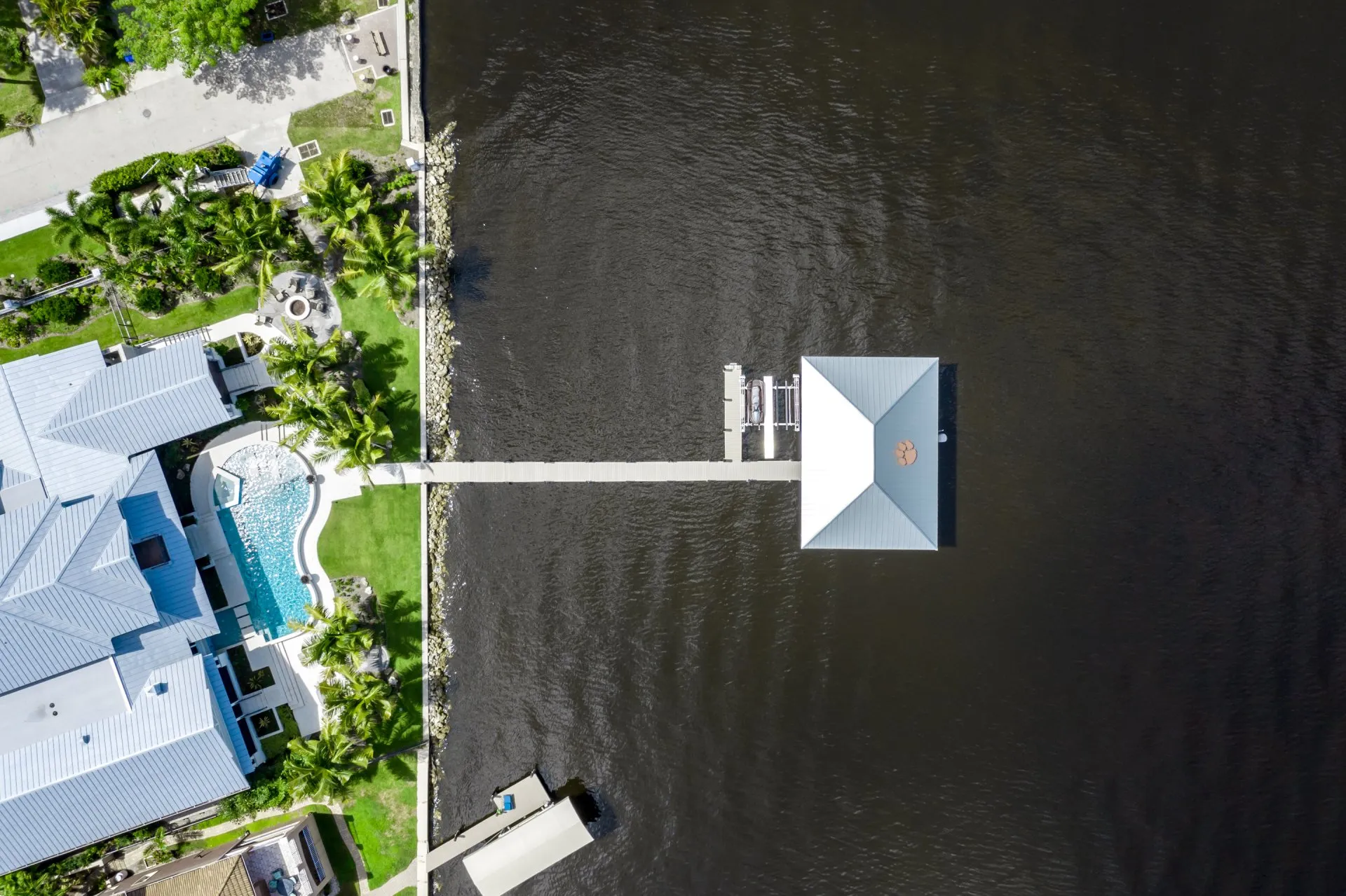 Aerial view of a dock with a covered boat house extending from a waterfront property.