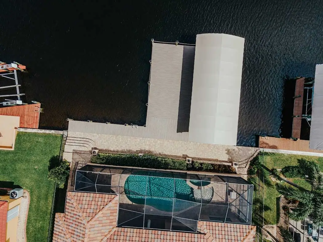 Aerial view of a dock with a covered section and a screened-in pool area beside a waterway.