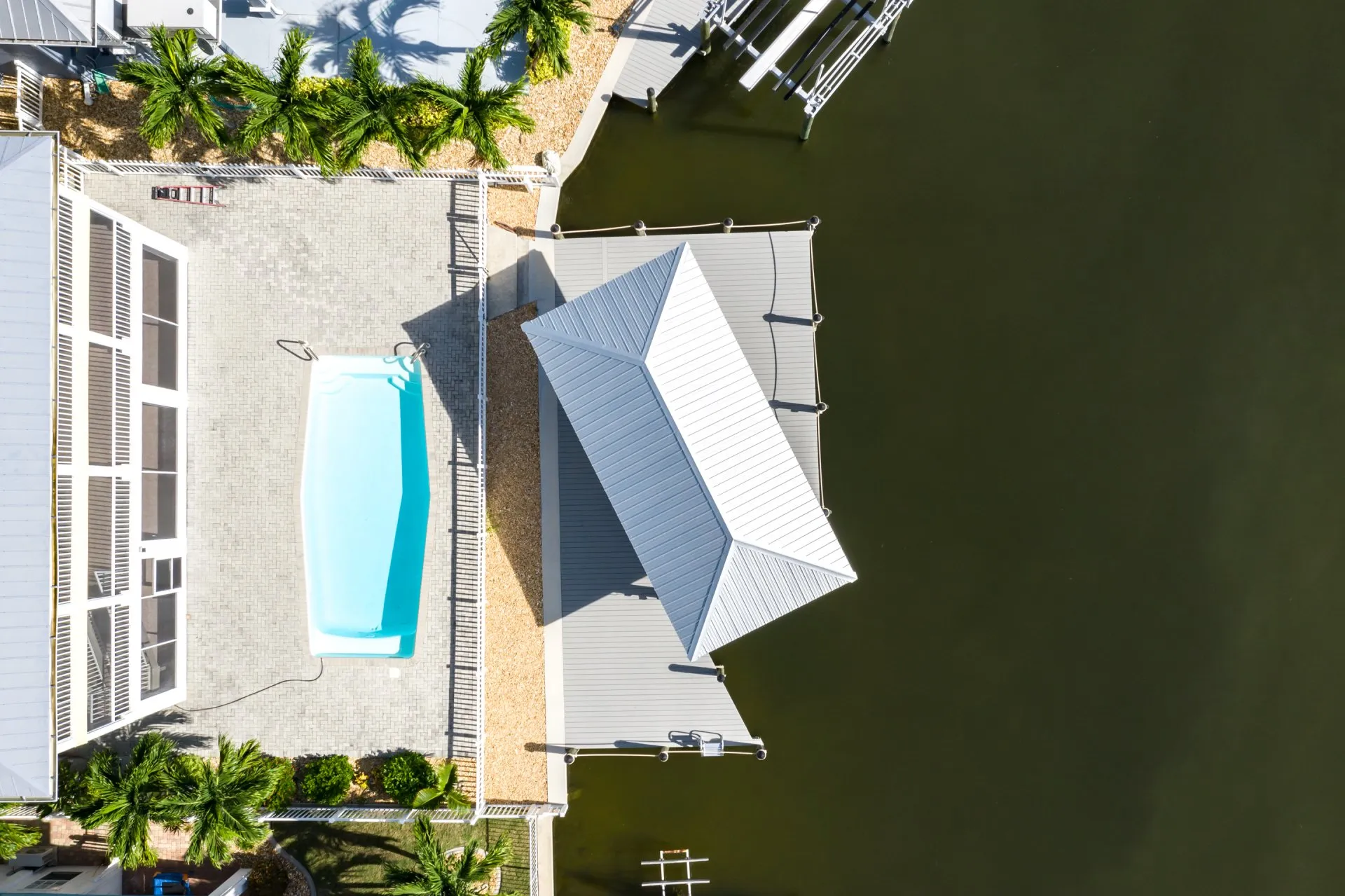 Aerial view of a waterfront home featuring a pool, covered dock, and tropical landscaping.