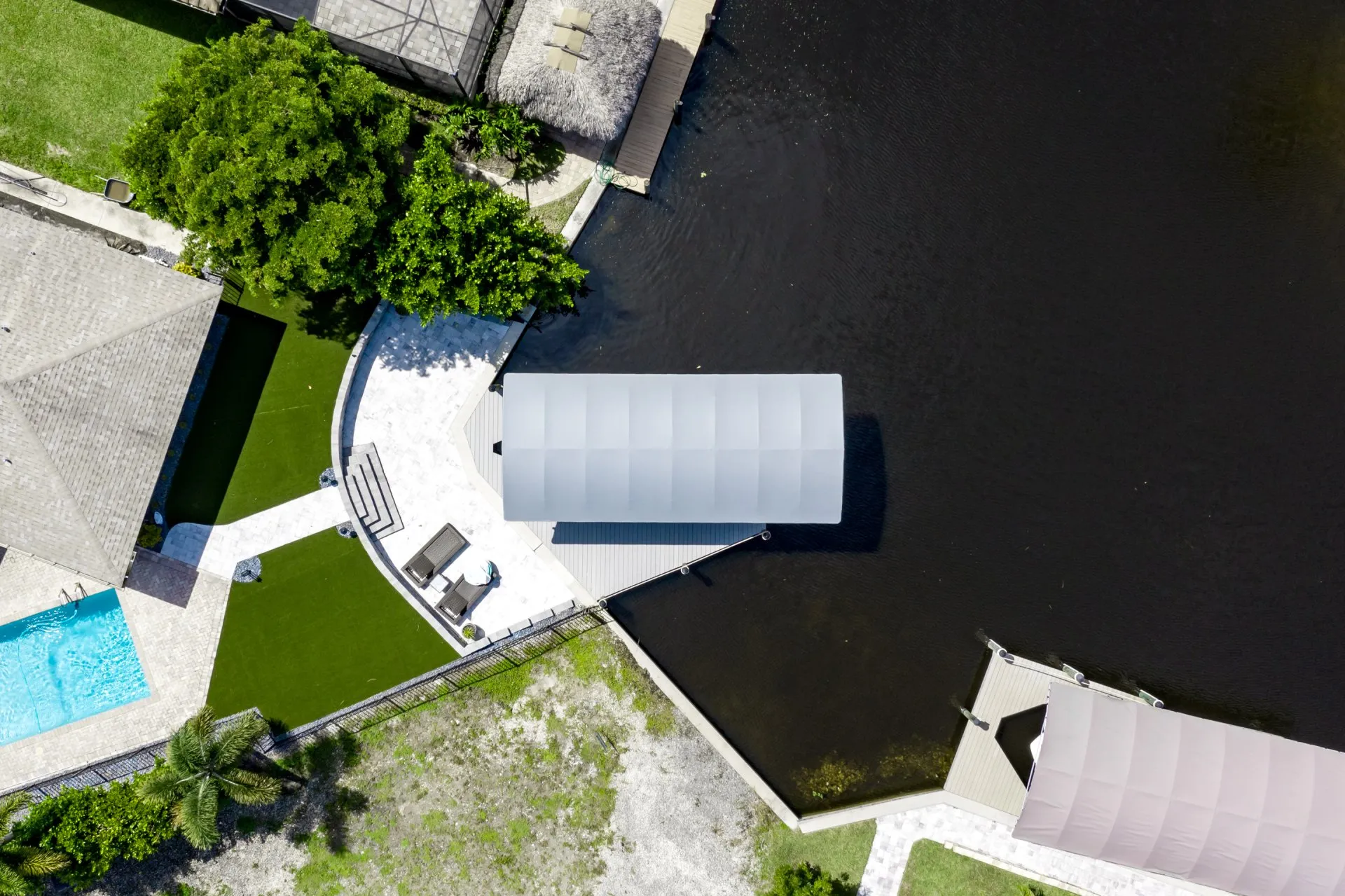 Aerial view of a landscaped backyard with a boat lift canopy and paved pathways by a canal.