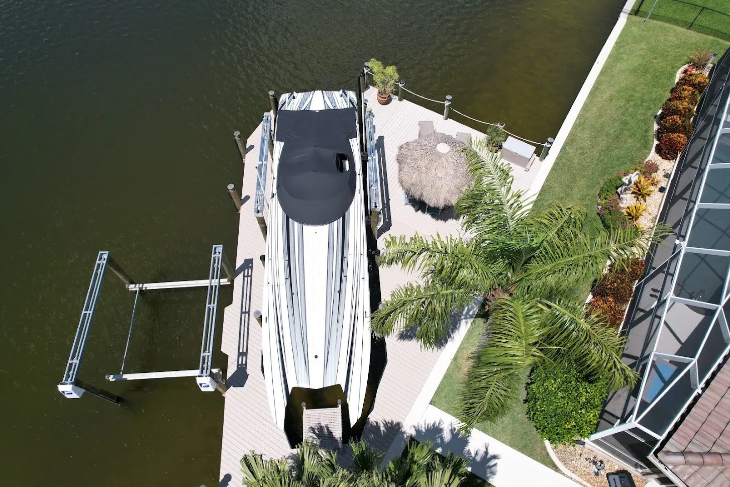 An aerial view of a custom dock with a boat lift, seating area, and tiki hut on a waterfront.