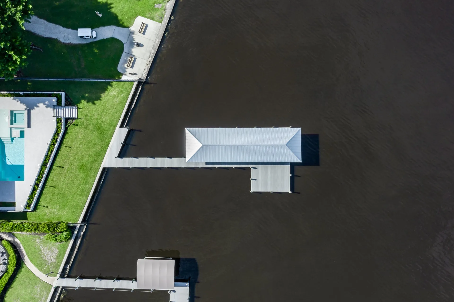 Aerial view of a dock with a metal roof extending over calm dark waters.