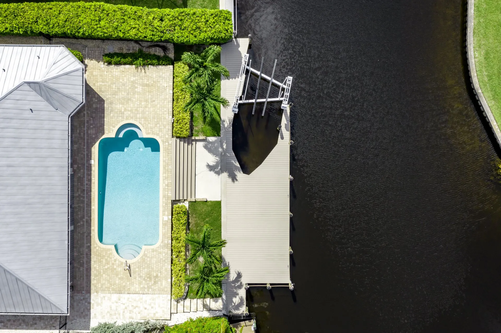 Aerial view of a dock on a canal beside a house with a pool and lush green landscaping.