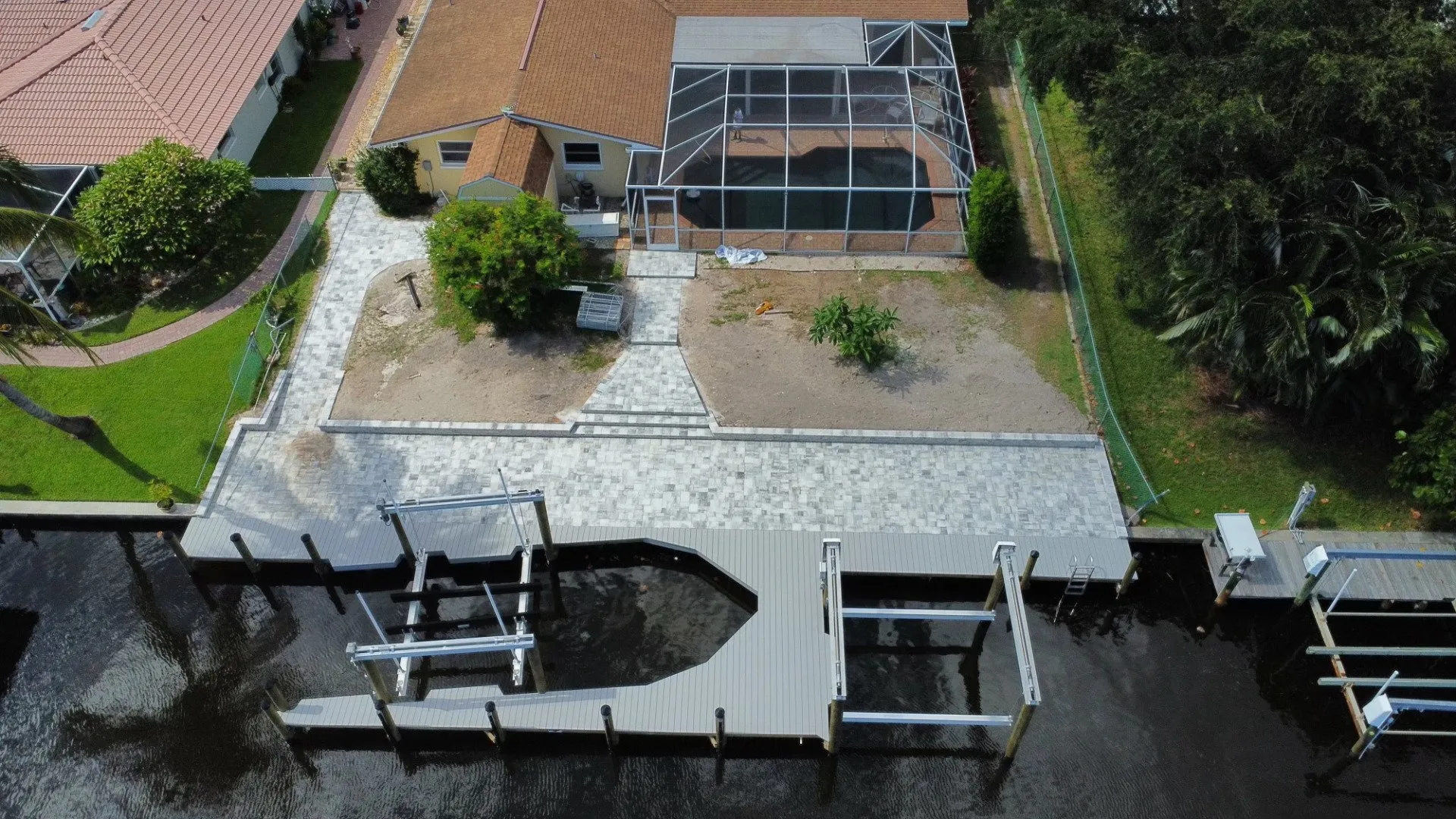 An aerial view of a waterfront home with a newly constructed paver walkway and custom dock along a canal.