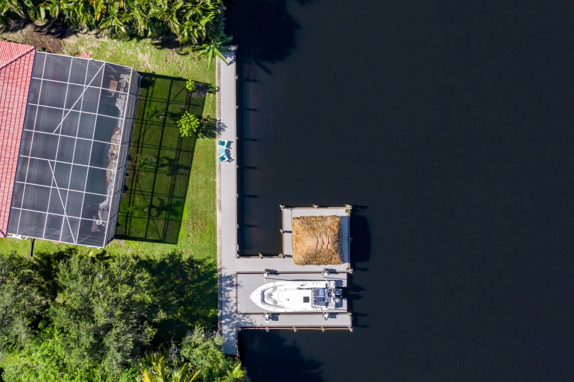 Aerial view of a waterfront property featuring a dock with a boat and tiki hut.