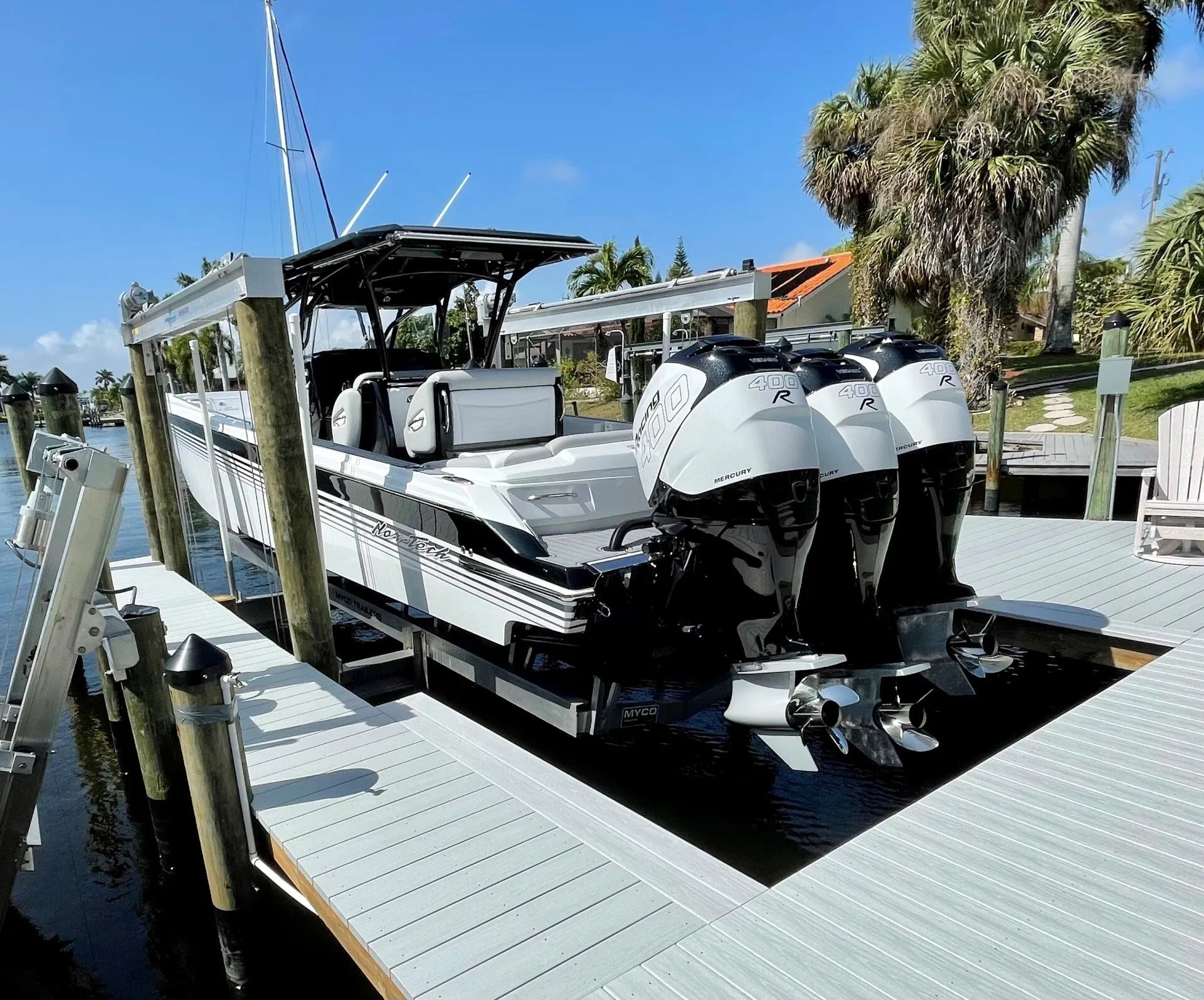 A sturdy aluminum boat lift system between docks in a residential canal with palm trees in the background.