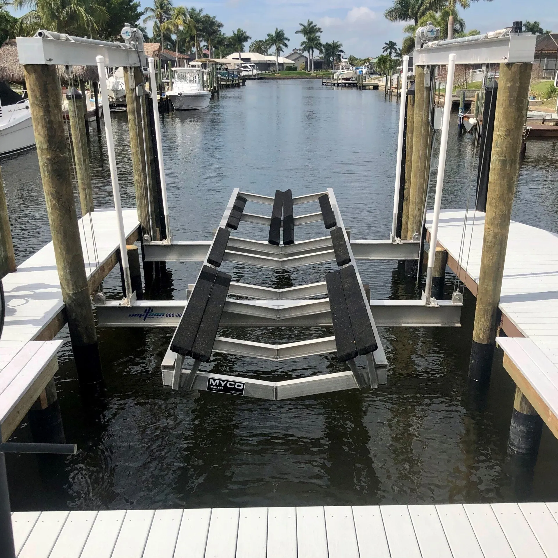 A sturdy aluminum boat lift system between docks in a residential canal with palm trees in the background.