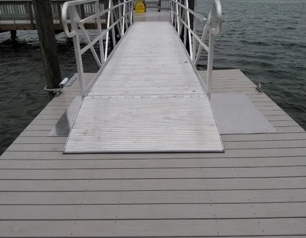 Aluminum gangway with railings connecting a dock to a floating platform over calm waters.