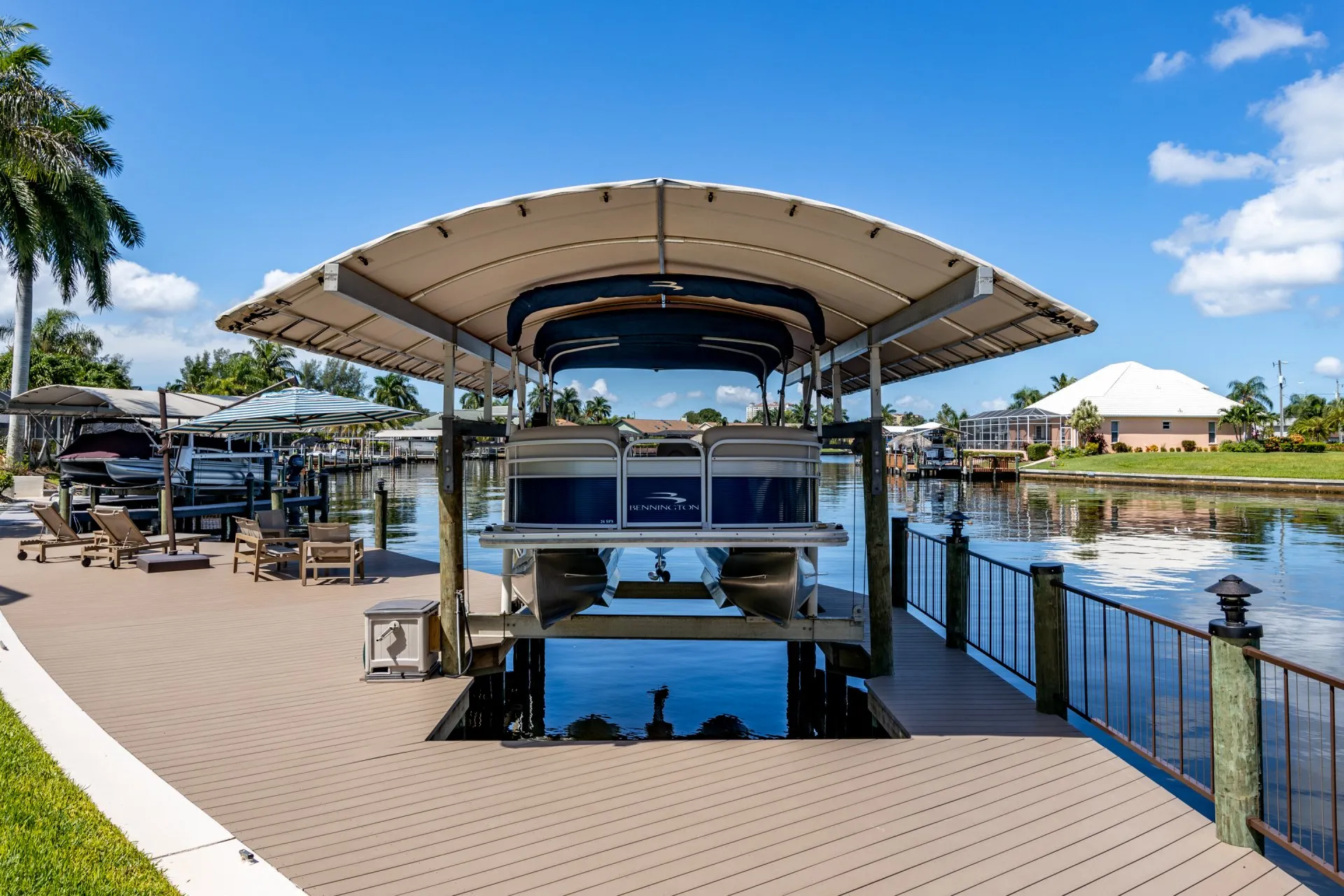 Bennington pontoon boat elevated on a covered boat lift with a canal backdrop and wooden dock.