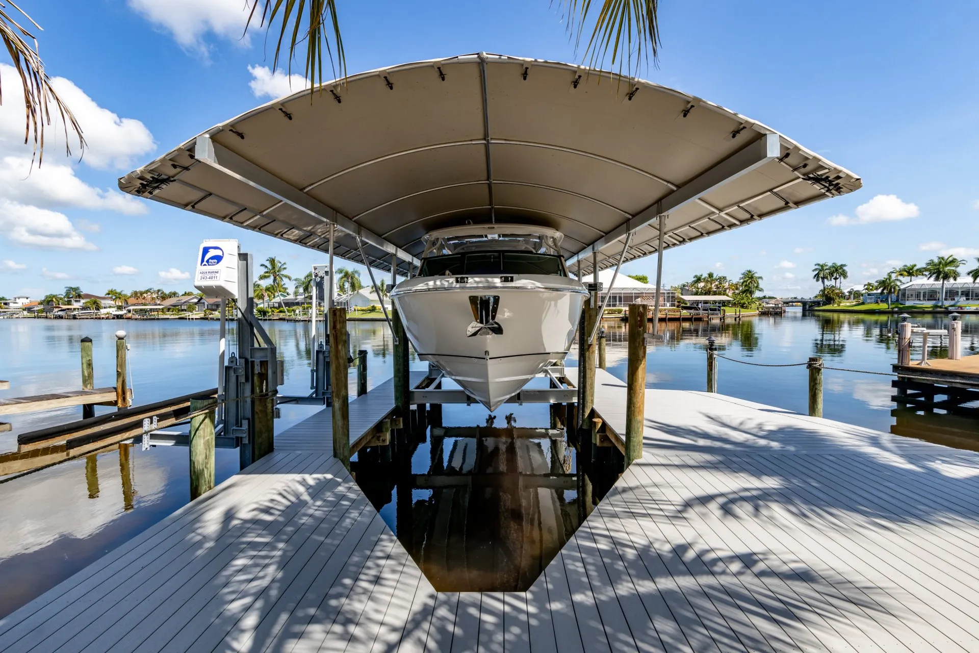 A boat secured on a lift under a canopy at a dock, overlooking a tranquil canal.