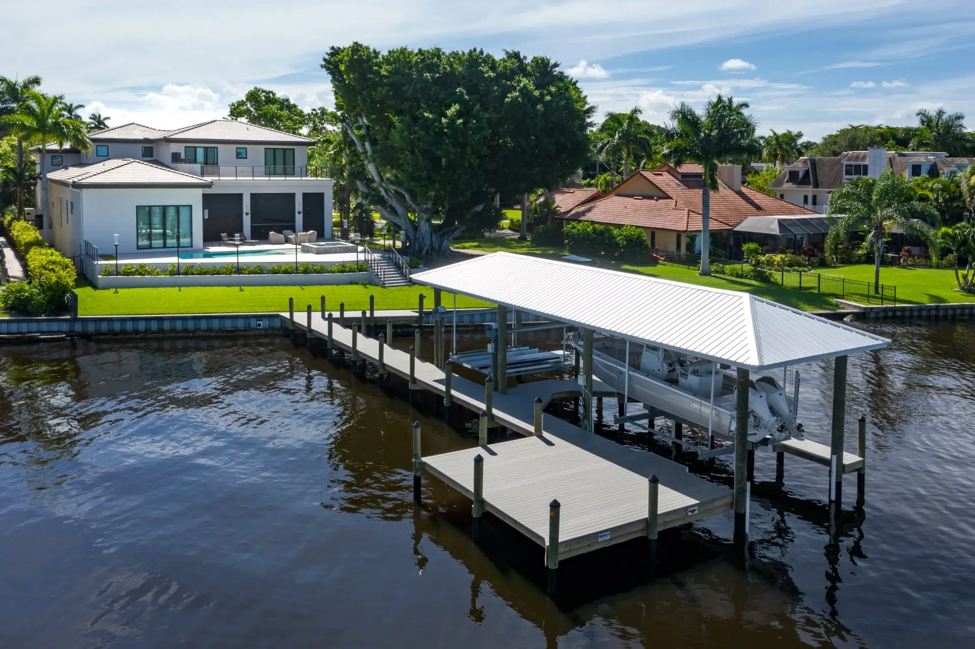 Luxury waterfront property with a covered dock, boat lift, and manicured landscaping along a serene canal.