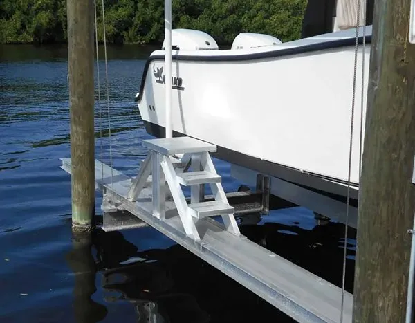 Boat lift with attached aluminum steps and walkway for easy access to a white vessel.