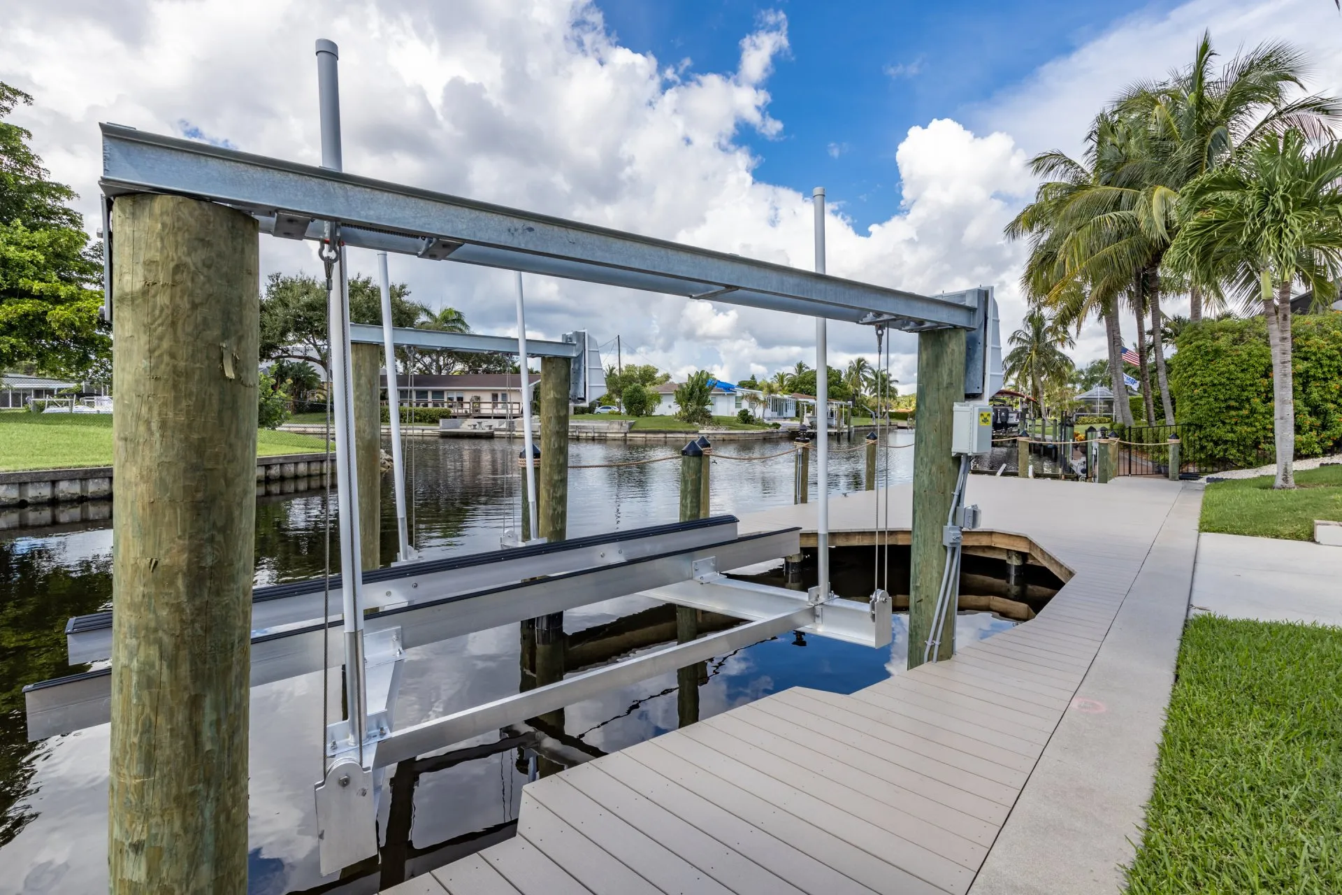 A boat lift on a dock along a serene residential canal, framed by palm trees and lush greenery.