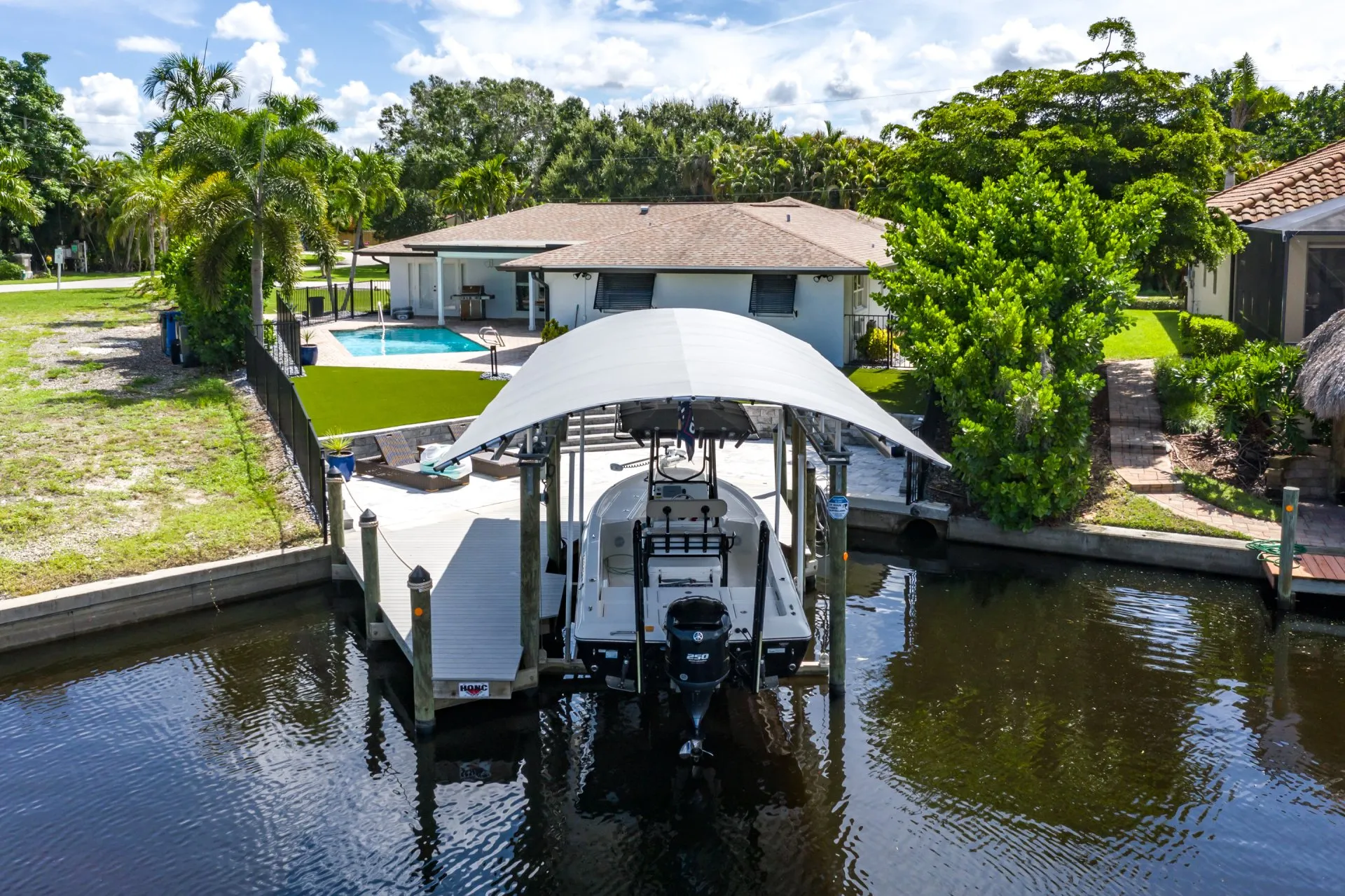 Backyard with a boat lift featuring a canopy, a swimming pool, and lush landscaping by a canal.