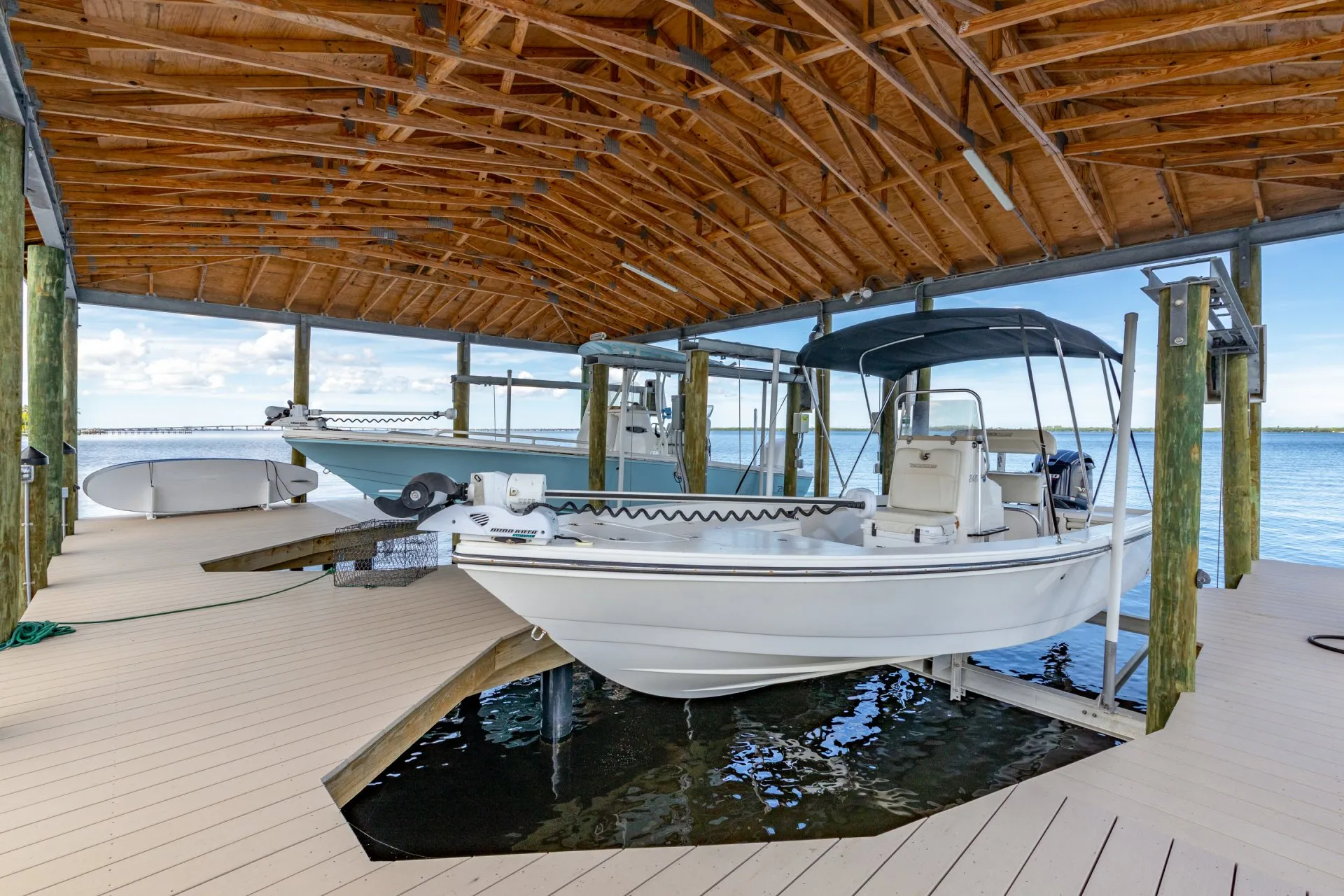 A white boat secured on a lift under a wooden covered dock overlooking the water.