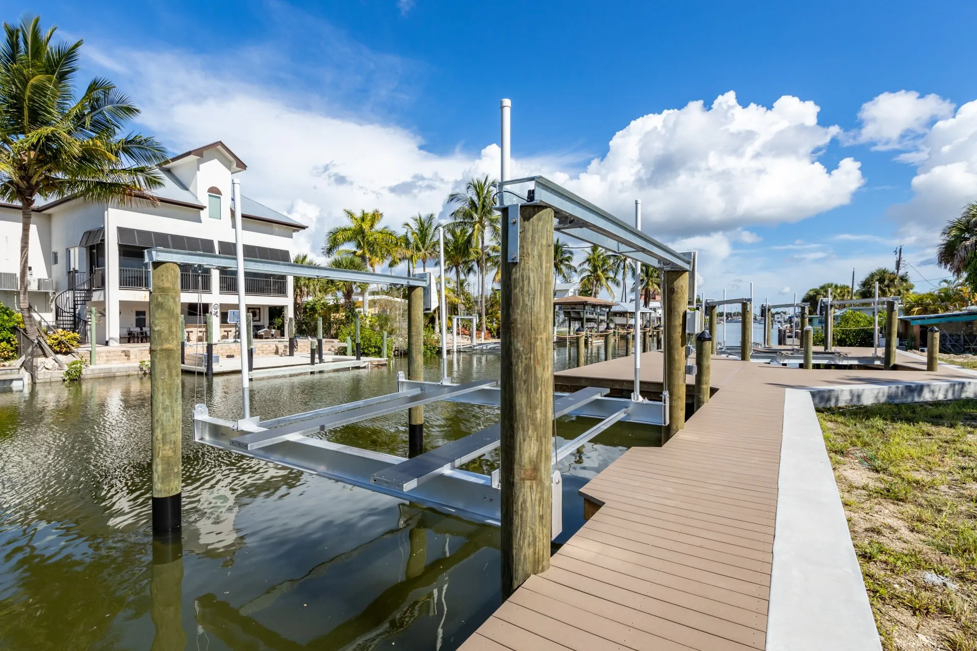 A boat lift on a modern dock along a residential canal, surrounded by palm trees and waterfront homes.