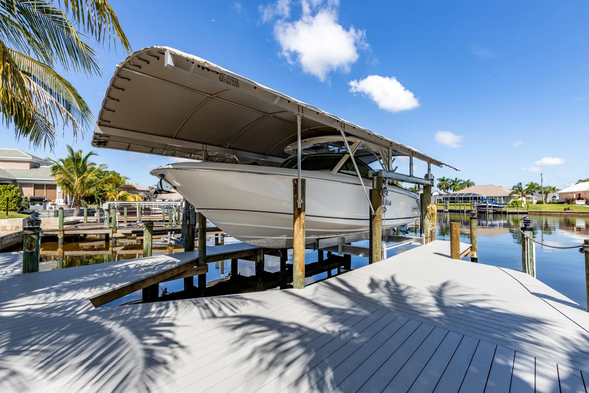 A boat resting on a lift under a canopy, surrounded by a calm waterfront dock.