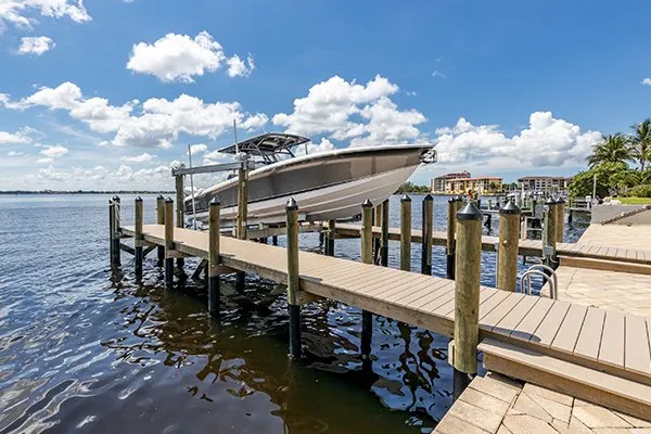 A dockside view showcasing a boat lift holding a boat over the water with nearby buildings in the background.