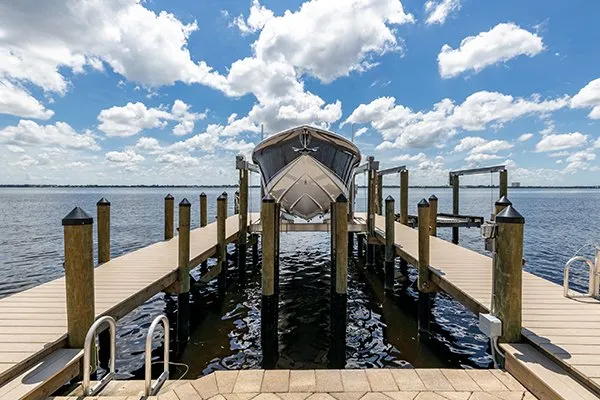 A frontal view of a boat lifted above the water by a waterfront dock system with a bright sky overhead.