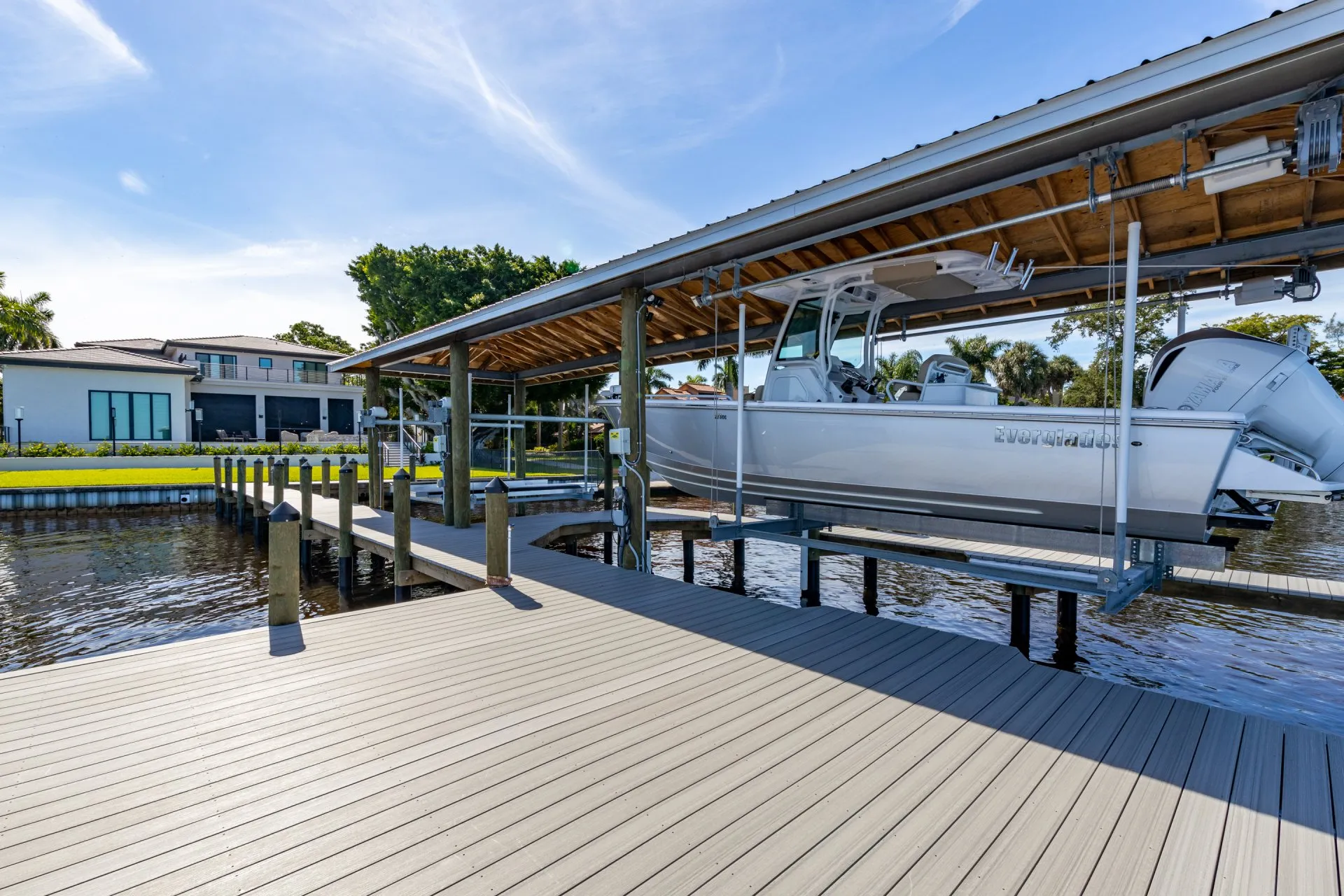 A modern boat lifted on a dock system with a wooden shelter and a waterfront home in the background.