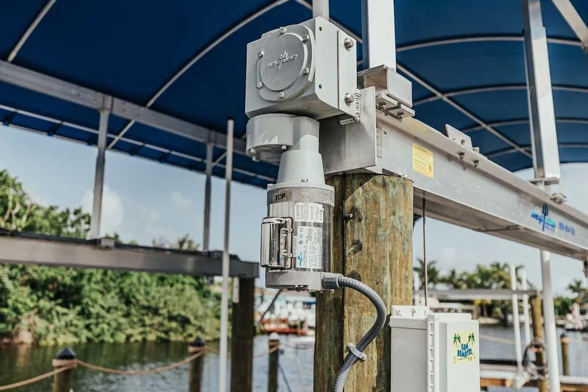 A close-up of a boat lift motor and control system mounted on a wooden piling under a canopy.