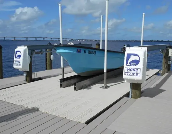 Blue boat resting on a boat lift with motorized controls and composite decking overlooking the water.