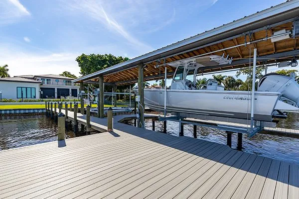 Covered dock with a boat lift holding a white motorboat over a calm waterway.