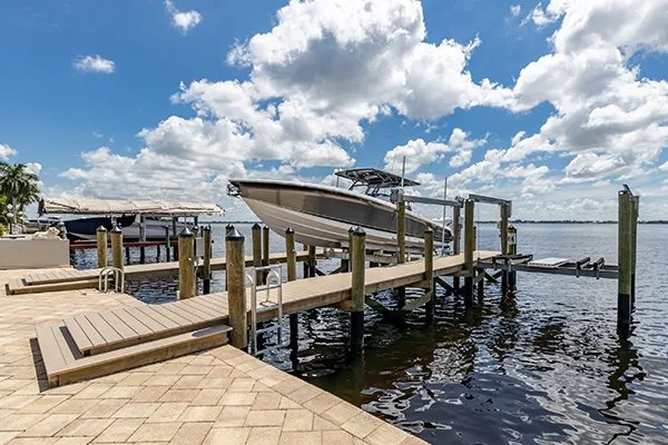 A waterfront dock featuring a boat lift holding a large boat against a backdrop of blue skies and clouds.