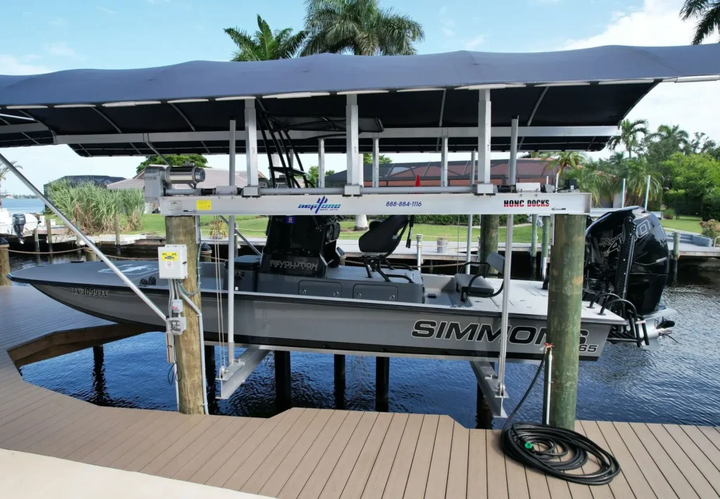 A boat securely lifted on a covered boat lift over a canal, with a Simmons logo on the side of the boat and a well-maintained dock below.