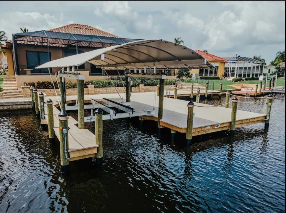 Canal dock with a curved canopy, boat lift, and composite decking near a waterfront home.