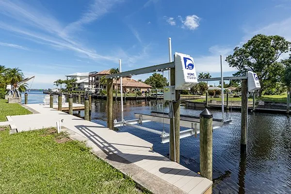 A canal-side dock featuring multiple boat lifts installed along a well-maintained pathway under a clear sky.