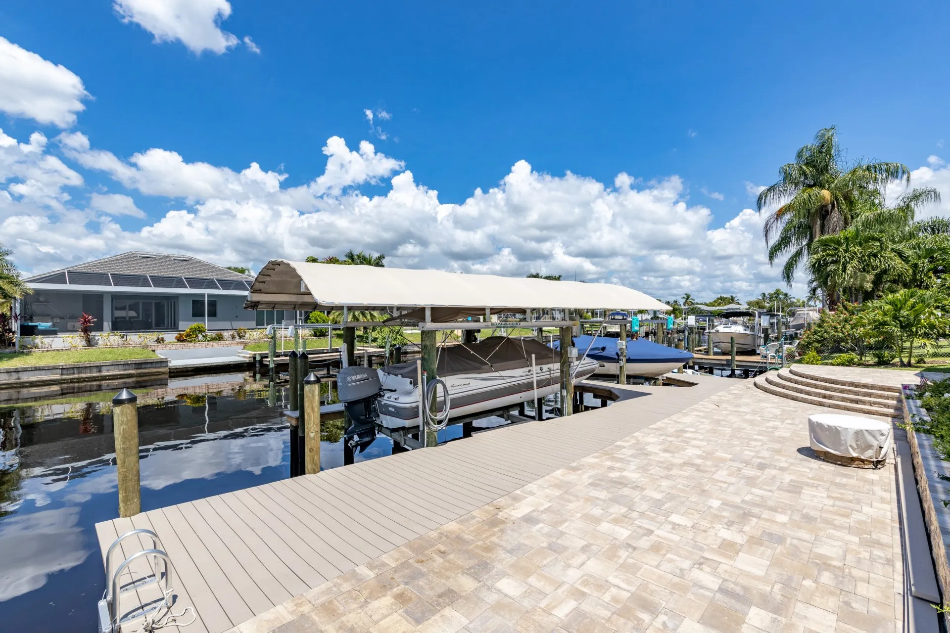 A covered boat lift dock with a paved walkway alongside a peaceful residential canal.