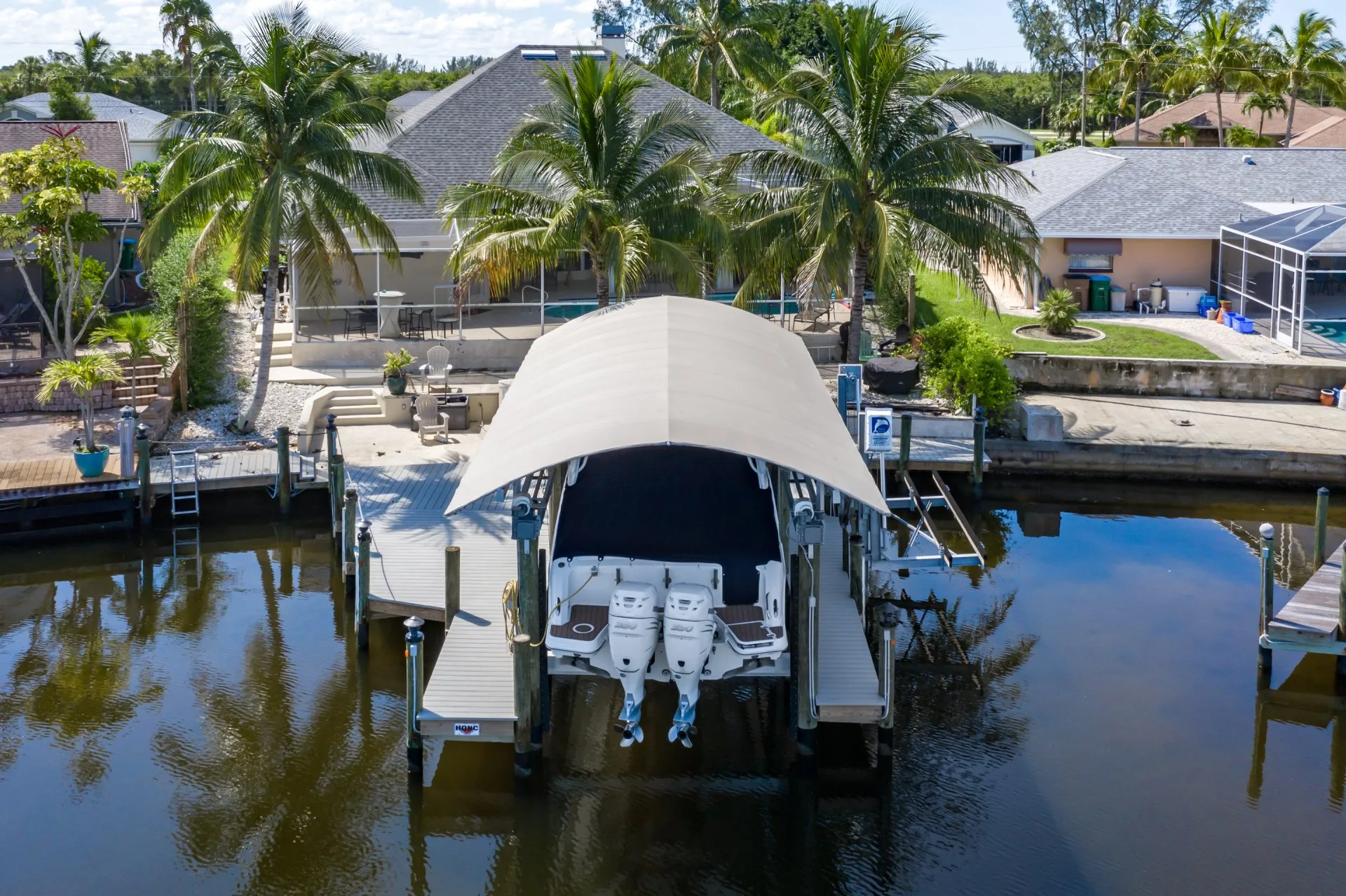 A covered boat lift with dual outboard engines docked near a waterfront home.