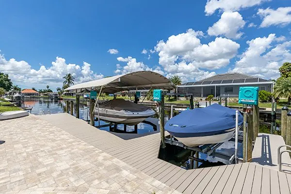 A canal-side dock featuring two covered boat lifts, each holding boats securely under protective canopies.