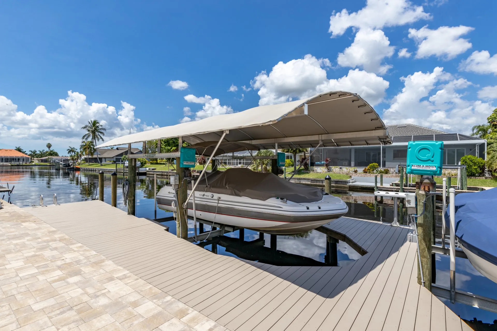 A covered boat resting on a lift at a dock, featuring a shade canopy and a serene canal view.