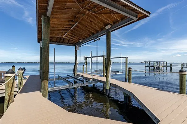 A waterfront dock featuring a covered boat slip and open boat lift, overlooking calm waters on a sunny day.