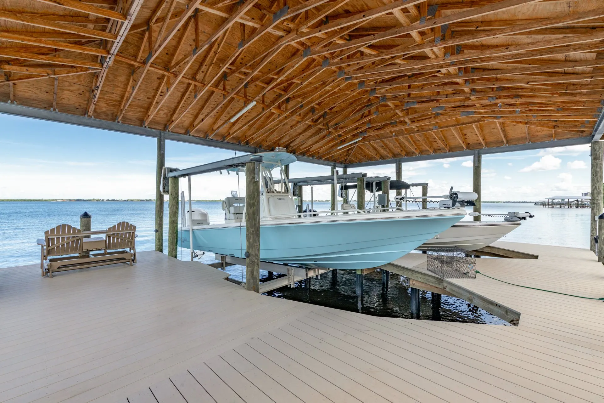 A light blue boat on a lift under a wooden covered dock with a waterfront view.