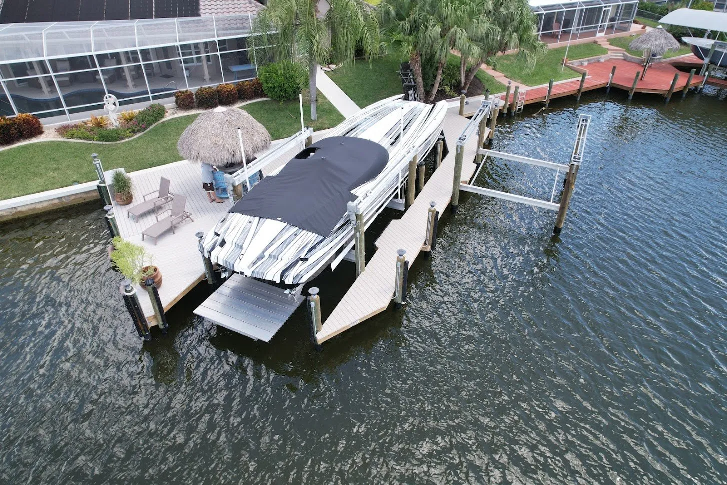 A custom boat dock with a covered boat lift, seating area, and a tiki hut overlooking the water.