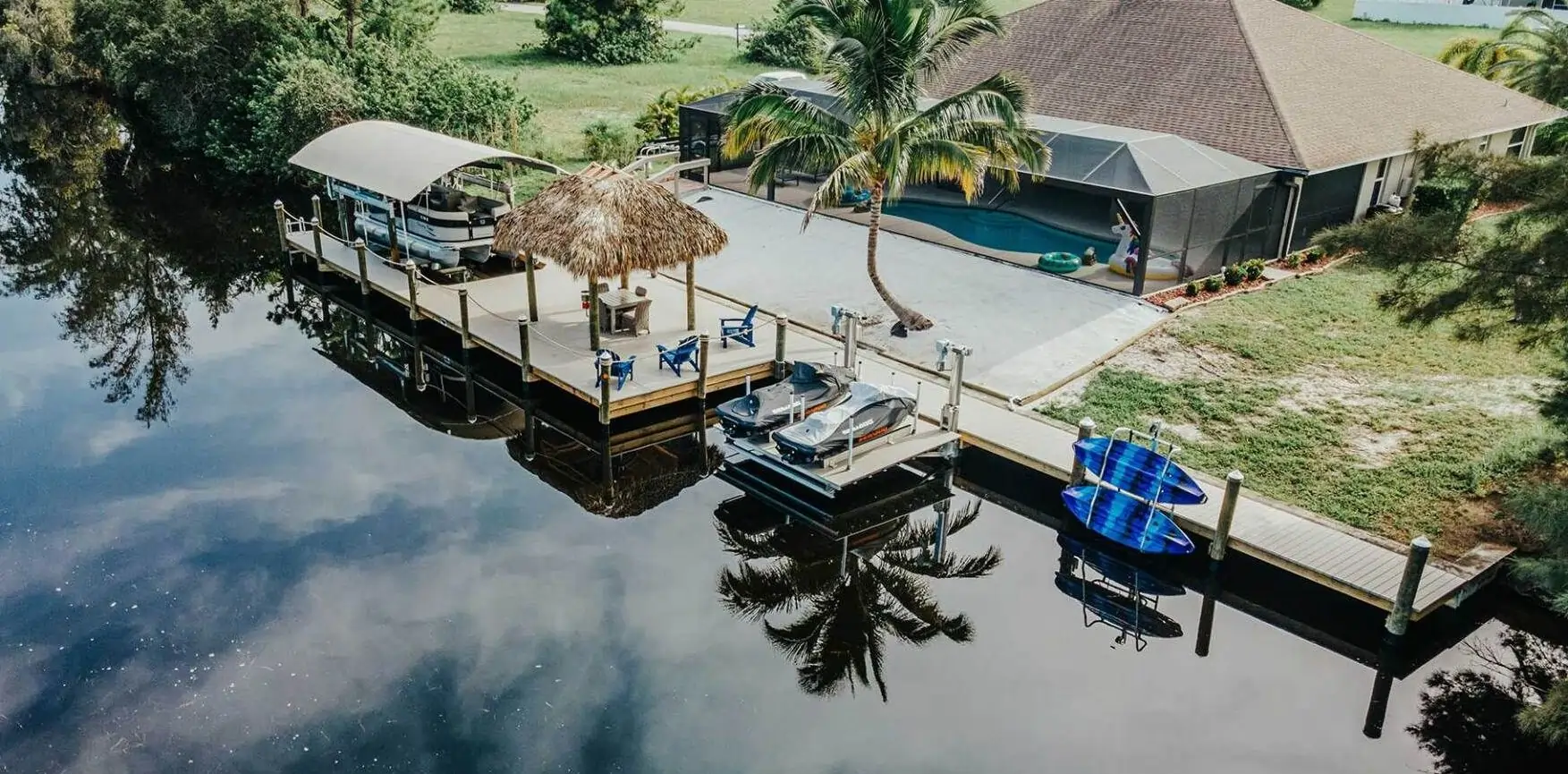 A cozy dock setup with a tiki hut, boat lifts, and lounge seating by a tranquil waterway.