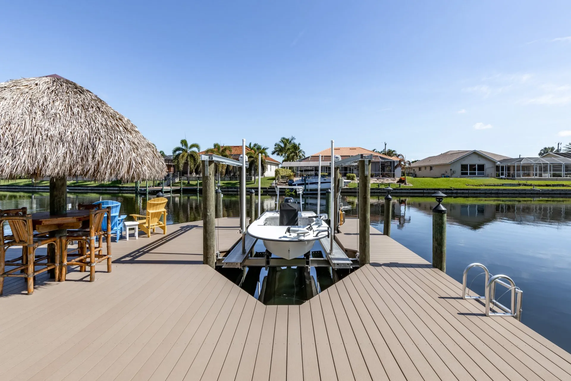 Boat lift with a small vessel, surrounded by a dock with a tiki hut and vibrant seating.