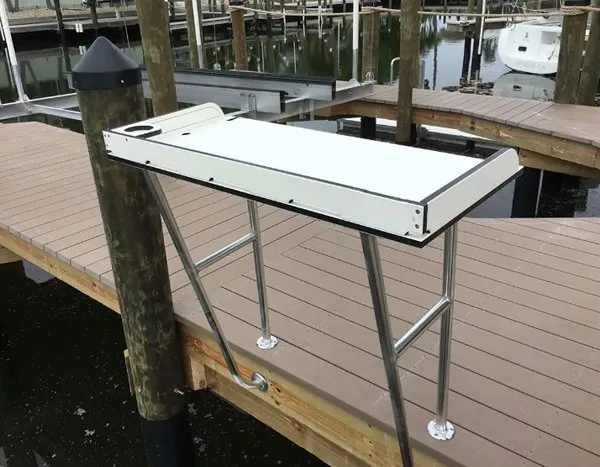 Side view of a dock-mounted fish cleaning station with a white tabletop and sturdy aluminum legs.