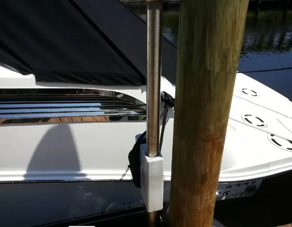 Close-up of a dock-mounted pole with protective padding next to a white boat with a black cover.