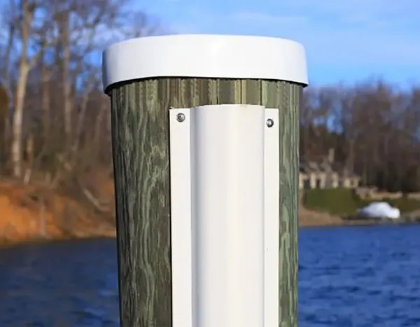 Wooden dock piling with a white cap and a mounted protective bumper along a waterfront.