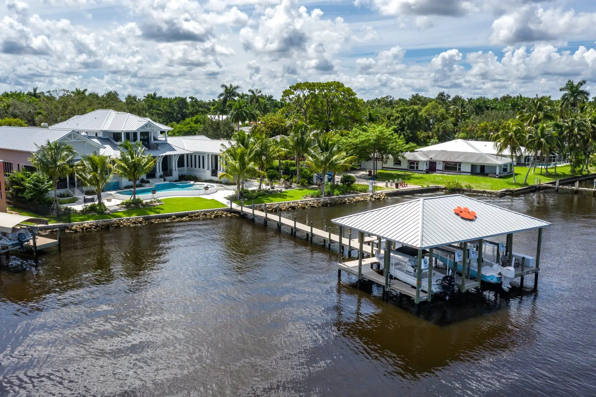 A luxurious waterfront home with a custom dock featuring a covered boat lift and tropical landscaping.