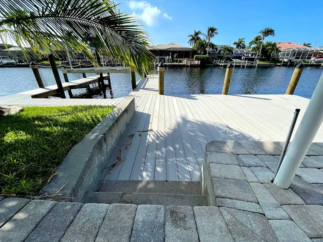 Concrete steps leading to a white wooden dock with a waterfront view surrounded by palm trees and pilings.