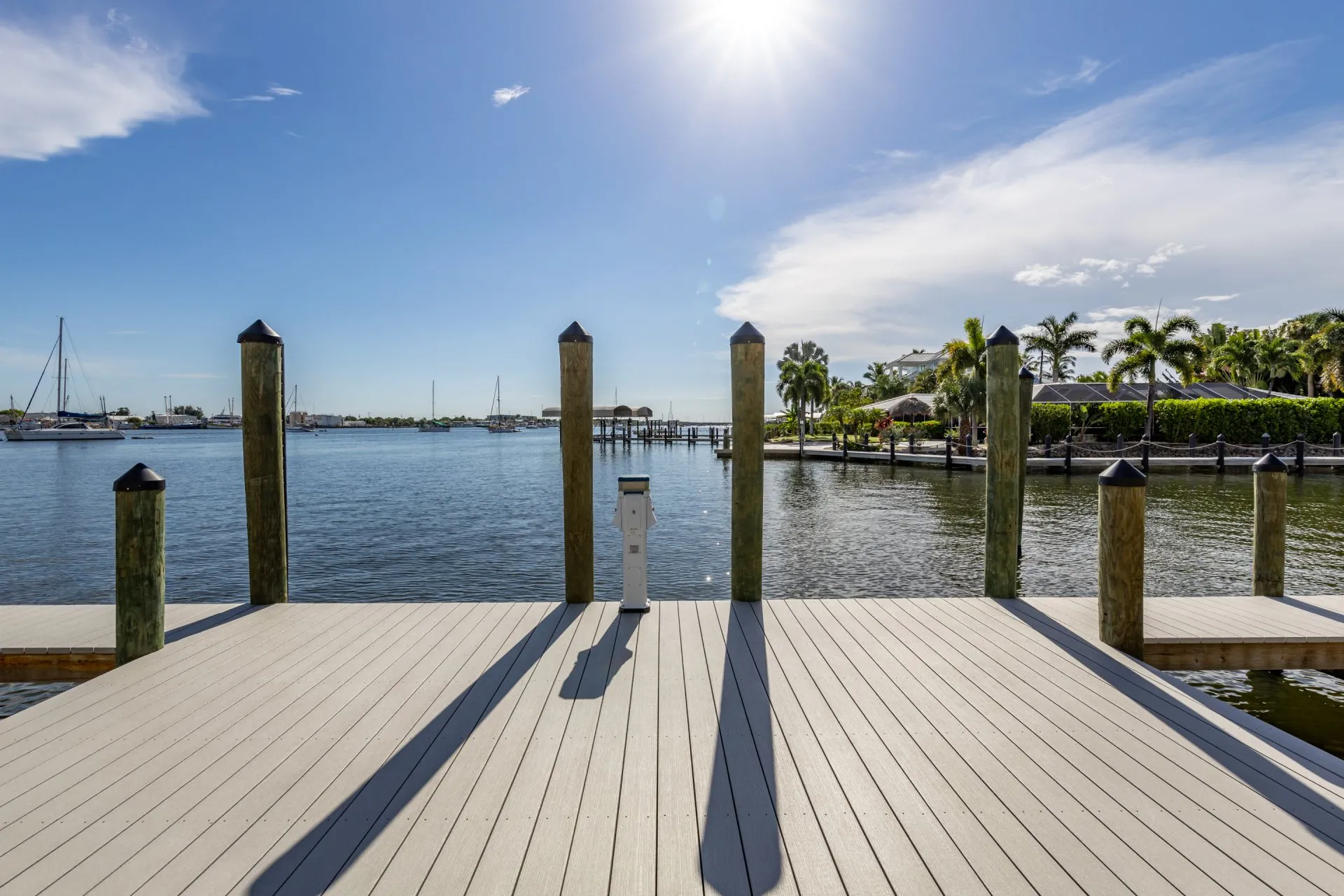 Sunny waterfront dock with wooden decking and mooring posts overlooking a calm marina.